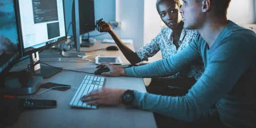 Zwei Personen sitzen vor einem PC-Arbeitsplatz und arbeiten an der Umsetzung